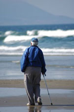Elderly man walking on beach with the aid of a standard cane Elderly man walking on beach with the aid of a standard cane